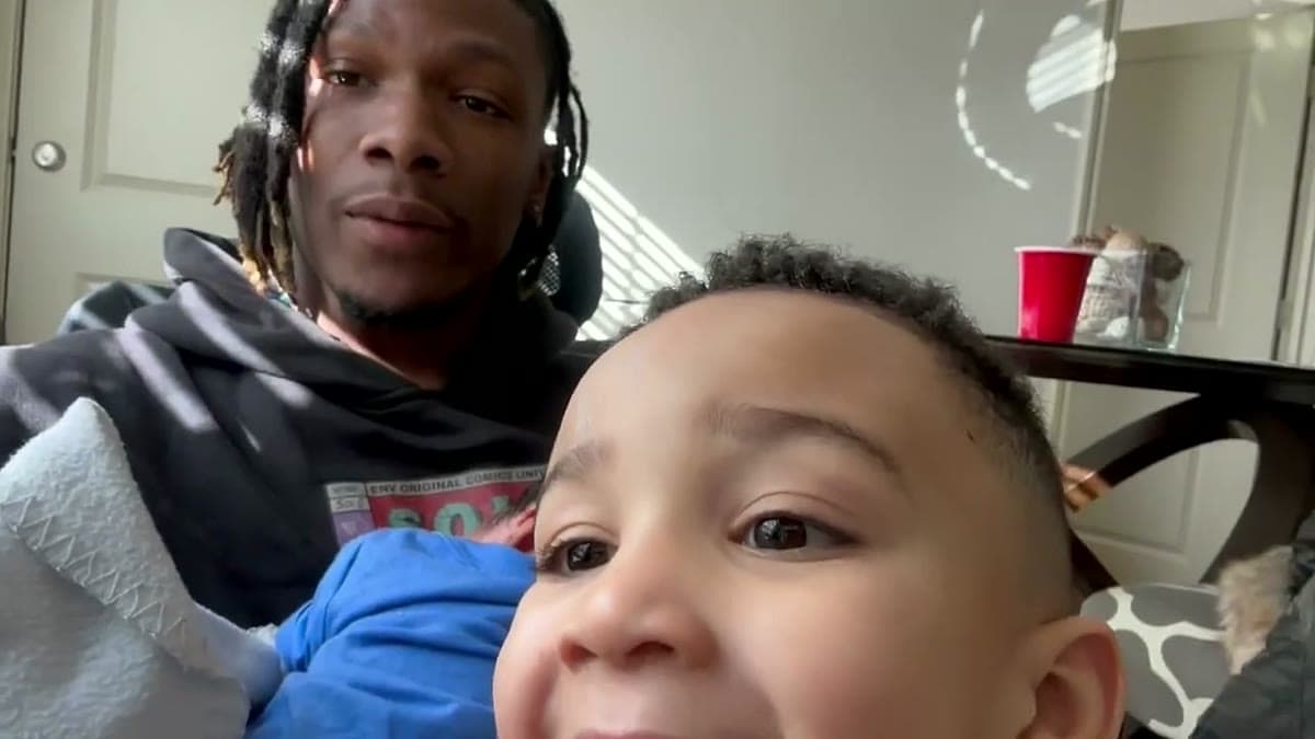 Uche holding a newborn nephew on his lap in the Airbnb while an older nephew leans into the camera