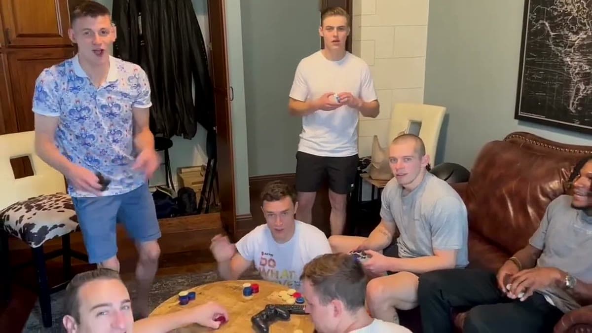 Groomsmen in a getting-ready suite before a wedding, sitting around a small table playing cards